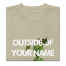 Zoomed-in view of a eucalyptus green T-shirt with bold white “Outside of Your Name” text and a green vine weaving through the letters. Clean neckline and heavyweight fabric texture visible.