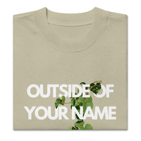 Zoomed-in view of a eucalyptus green T-shirt with bold white “Outside of Your Name” text and a green vine weaving through the letters. Clean neckline and heavyweight fabric texture visible.