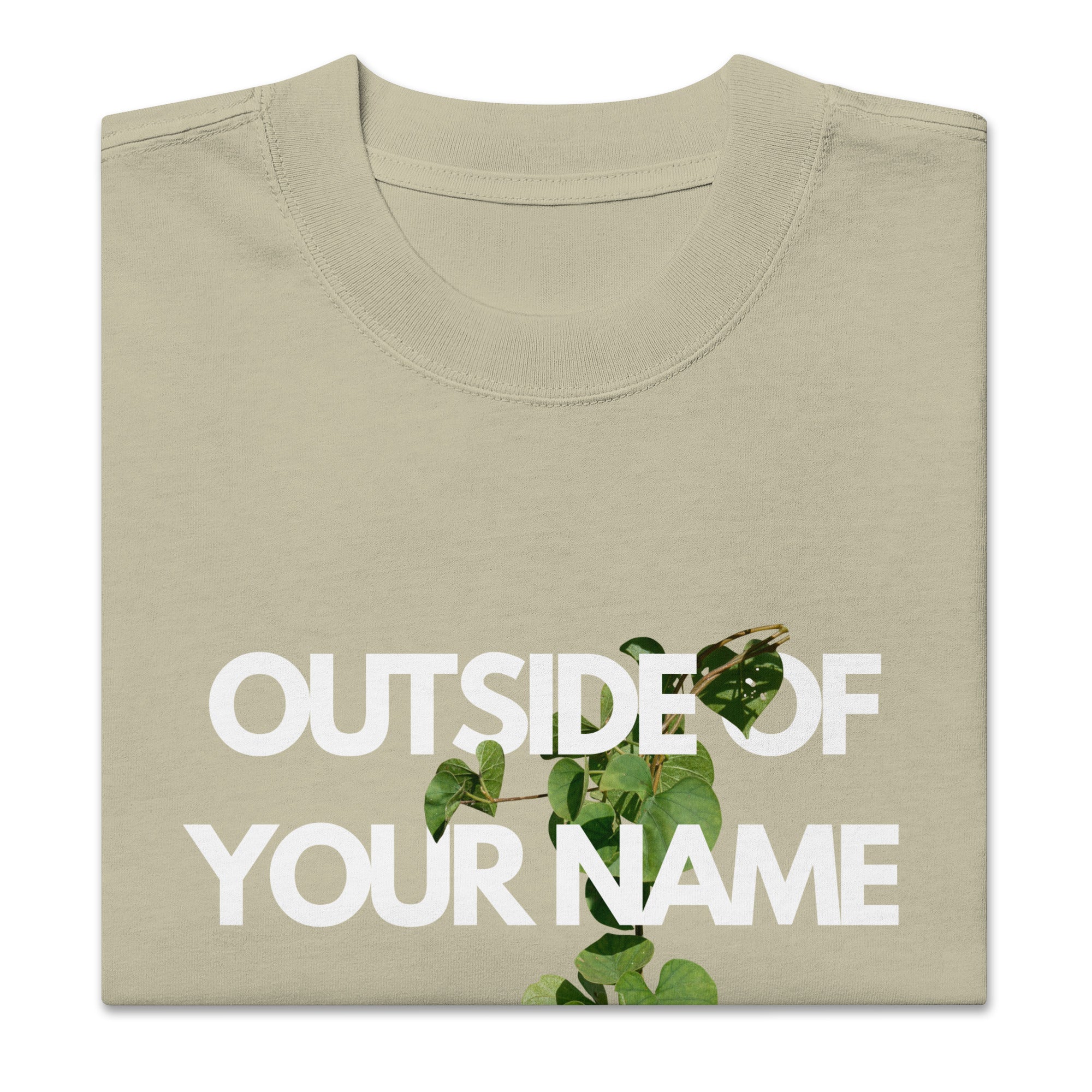 Zoomed-in view of a eucalyptus green T-shirt with bold white “Outside of Your Name” text and a green vine weaving through the letters. Clean neckline and heavyweight fabric texture visible.